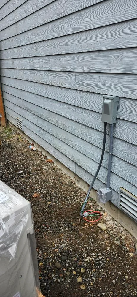Heat pump electrical disconnect and conduit on a home’s exterior wall beside a new outdoor unit in Lake Forest Park, WA