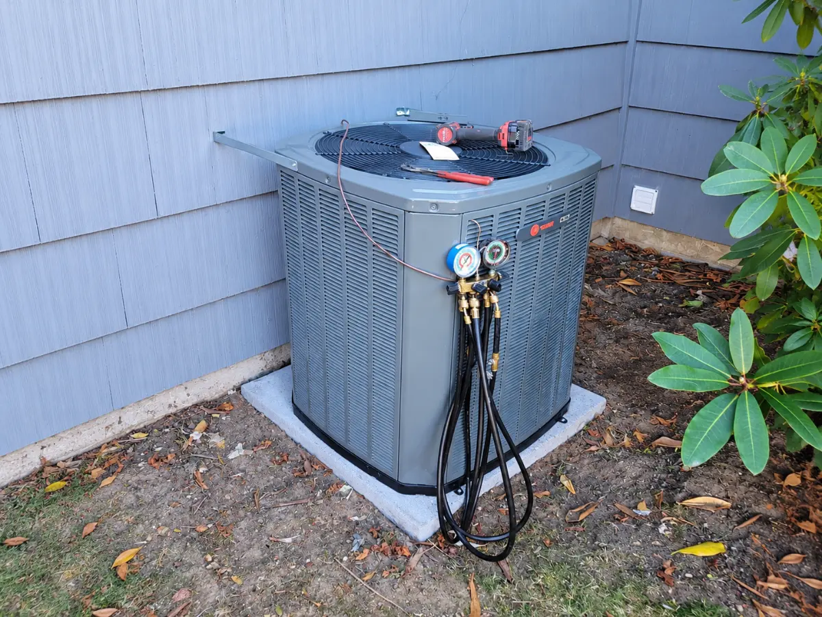 Outdoor HVAC unit with manifold gauges connected during refrigerant service.