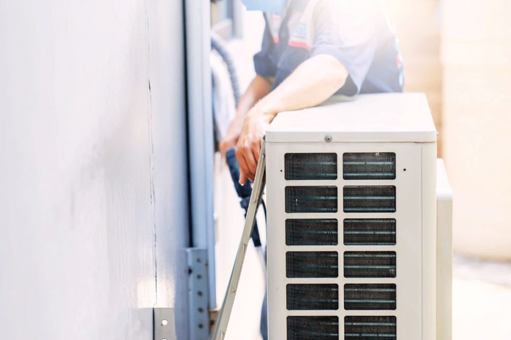 A man in a blue shirt performing air conditioner maintenance.