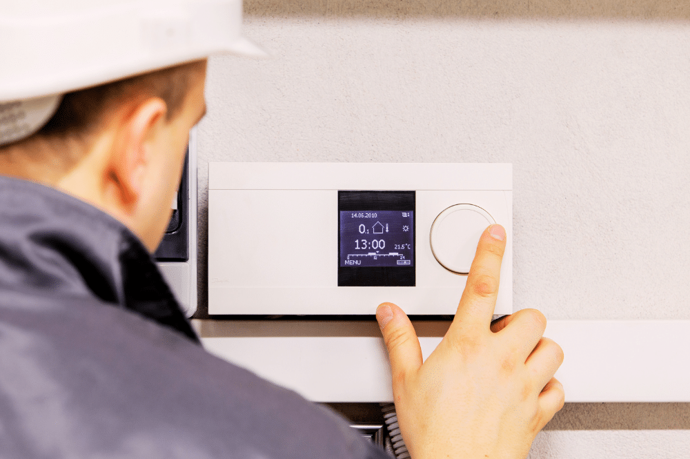 A man in a hard hat pointing working on a thermostat, demonstrating smart HVAC solutions.