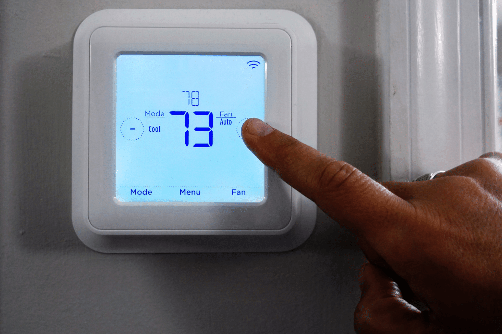 Hand adjusting thermostat on wall for efficient home cooling.