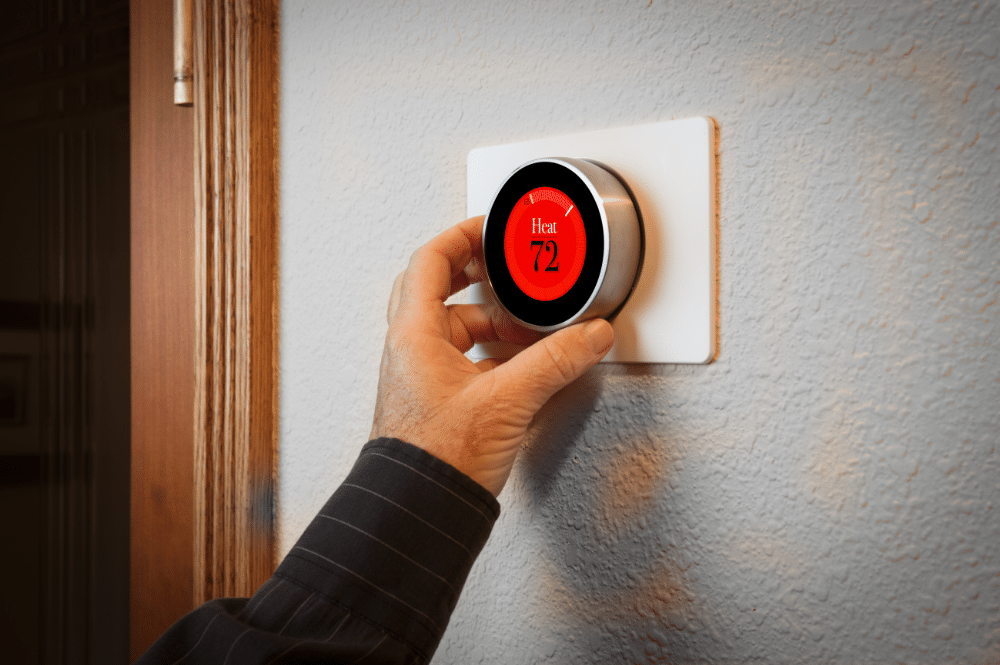 A person adjusts the wall thermostat, optimizing home heating solutions for comfort and energy efficiency.